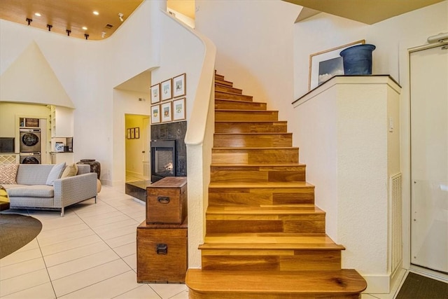 staircase featuring recessed lighting, a high ceiling, stacked washer / dryer, a multi sided fireplace, and tile patterned floors