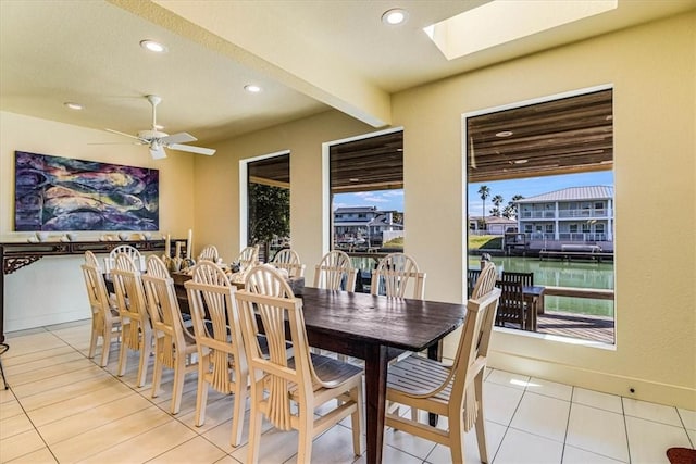 dining room with a skylight, baseboards, a ceiling fan, a water view, and recessed lighting