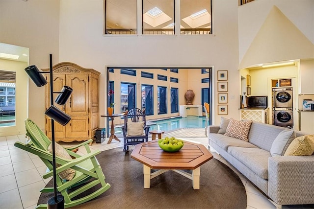 living room featuring a towering ceiling, stacked washing maching and dryer, a skylight, and light tile patterned flooring