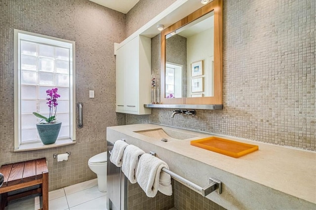 bathroom with tile walls, toilet, a sink, tile patterned flooring, and a wealth of natural light