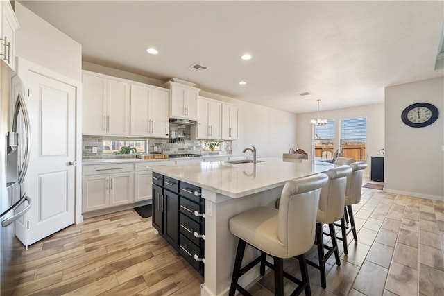 kitchen featuring an island with sink, appliances with stainless steel finishes, white cabinets, and decorative light fixtures