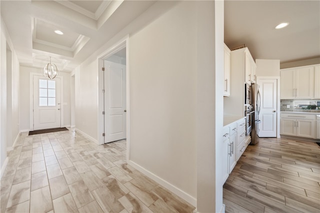 kitchen with appliances with stainless steel finishes, white cabinets, backsplash, crown molding, and an inviting chandelier