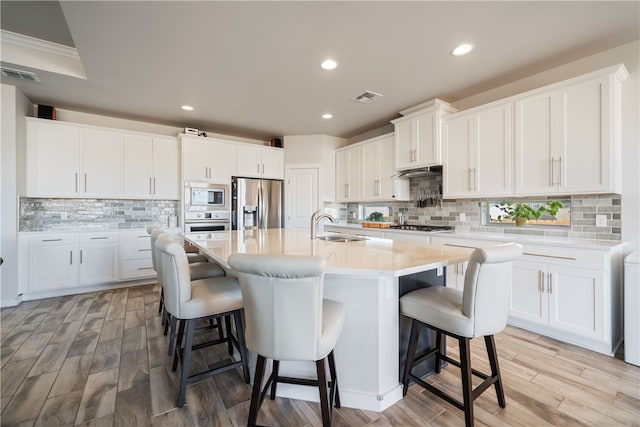 kitchen featuring a kitchen island with sink, stainless steel appliances, and white cabinets