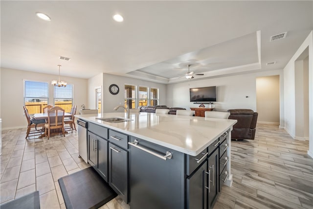 kitchen featuring a tray ceiling, sink, a center island with sink, and decorative light fixtures