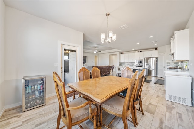 dining area featuring ceiling fan with notable chandelier, wine cooler, and light hardwood / wood-style flooring