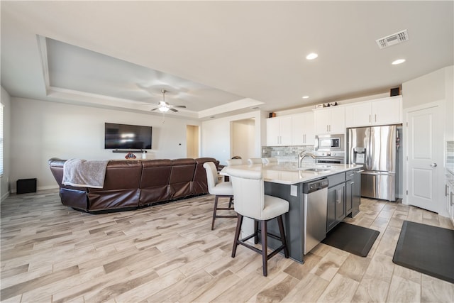 kitchen featuring appliances with stainless steel finishes, a kitchen island with sink, white cabinetry, a kitchen breakfast bar, and a raised ceiling