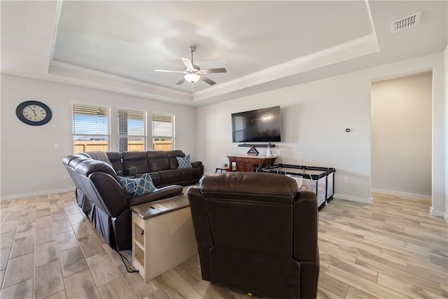 living room featuring ceiling fan, ornamental molding, a tray ceiling, and light hardwood / wood-style floors