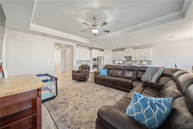 living room featuring ceiling fan, ornamental molding, and a tray ceiling