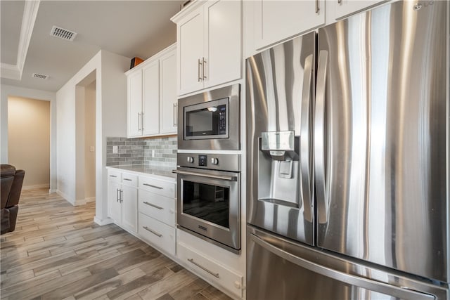 kitchen with tasteful backsplash, appliances with stainless steel finishes, light hardwood / wood-style floors, and white cabinets