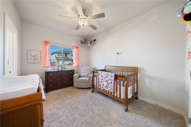 carpeted bedroom featuring ceiling fan and a crib