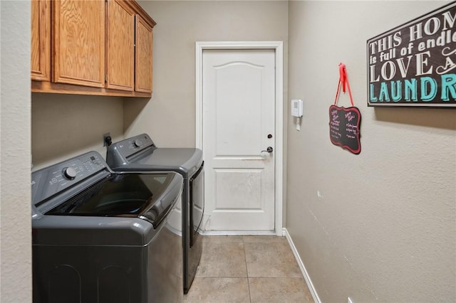 clothes washing area featuring light tile patterned floors, washing machine and dryer, and cabinets