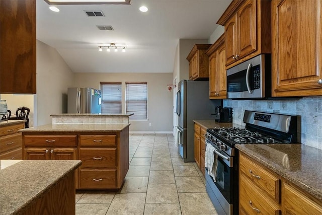 2618 Gentle Wind Ave, Corpus Christi, TX 78414 - kitchen featuring appliances with stainless steel finishes, decorative backsplash, brown cabinets, dark stone countertops, and a kitchen island