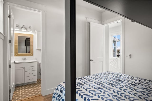 bedroom with light wood-type flooring, ensuite bath, and a sink