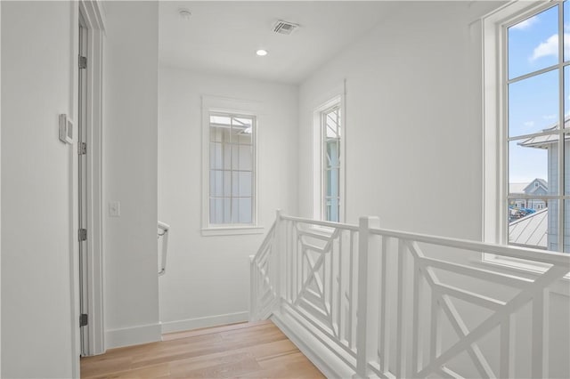 corridor with baseboards, light wood-style flooring, an upstairs landing, and a healthy amount of sunlight