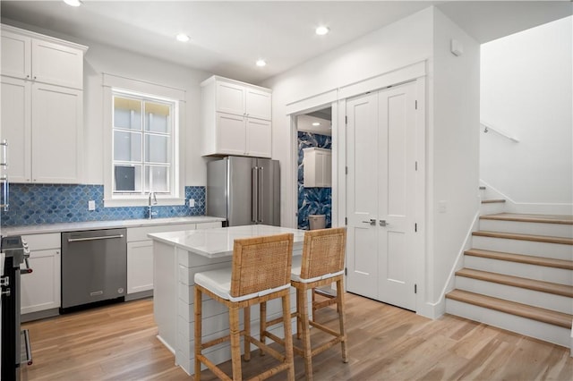 kitchen with light wood-style floors, tasteful backsplash, white cabinetry, and stainless steel appliances