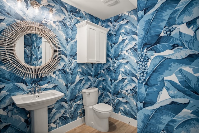 half bathroom with toilet, a sink, wood finished floors, baseboards, and wallpapered walls