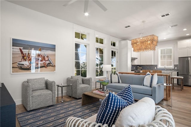 living area with visible vents, light wood-style flooring, baseboards, and ceiling fan with notable chandelier