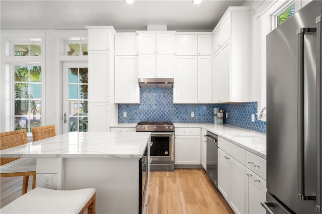 kitchen with decorative backsplash, a kitchen breakfast bar, stainless steel appliances, under cabinet range hood, and a sink