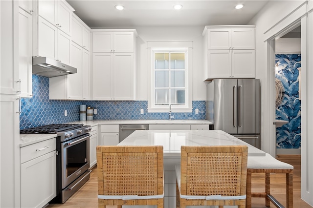 kitchen with high end appliances, white cabinetry, a sink, and under cabinet range hood