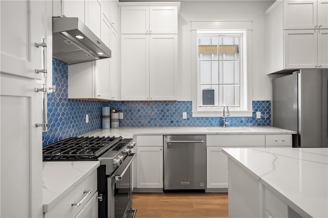 kitchen featuring wall chimney range hood, white cabinetry, appliances with stainless steel finishes, and a sink