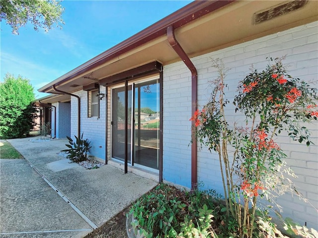 view of exterior entry with brick siding and a patio