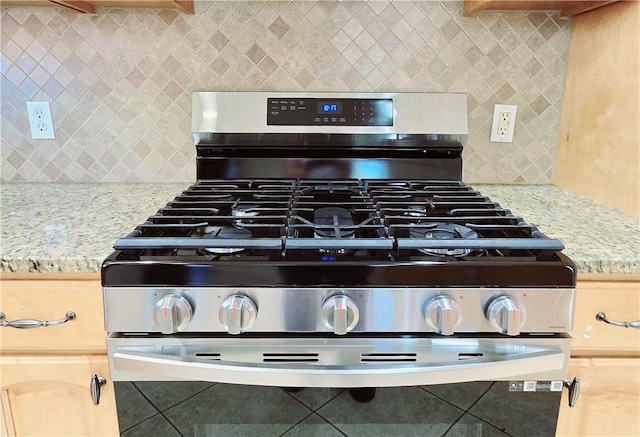interior details with stainless steel range with gas stovetop, tasteful backsplash, and light stone counters