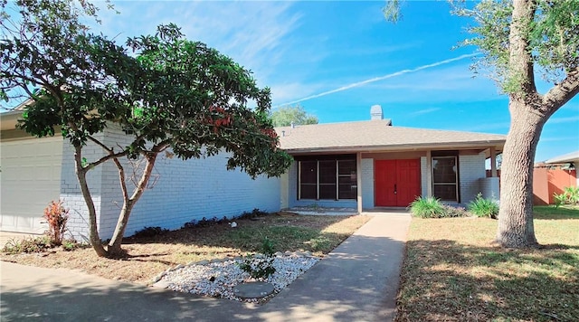 ranch-style home with a chimney, brick siding, and an attached garage