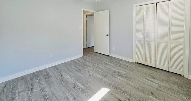 unfurnished bedroom featuring baseboards, wood finished floors, and a closet