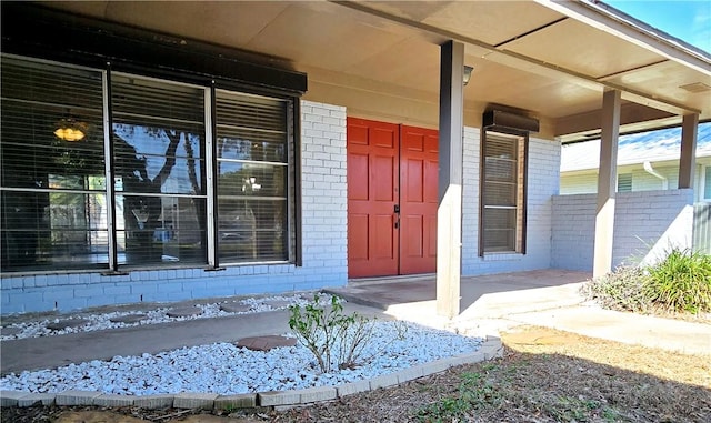 view of exterior entry featuring brick siding and a porch