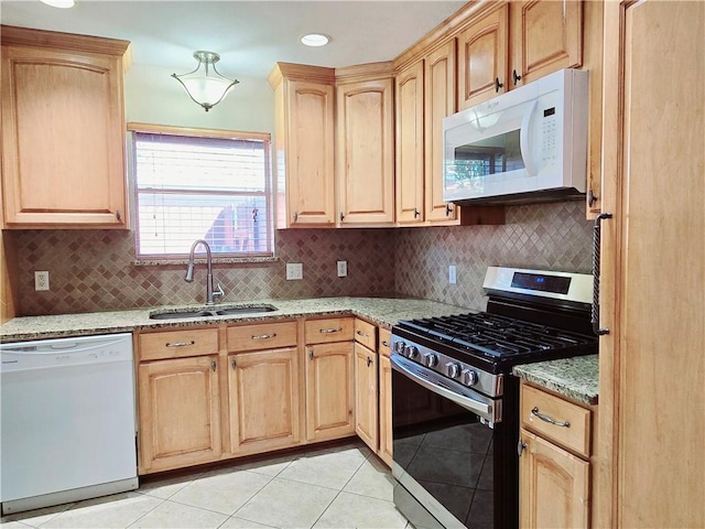 kitchen featuring white appliances, light brown cabinetry, light stone countertops, and a sink