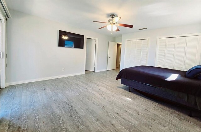 bedroom with a ceiling fan, wood finished floors, multiple closets, baseboards, and visible vents