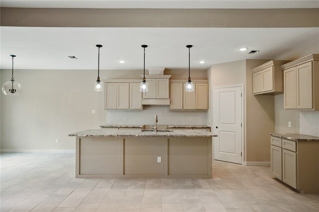 kitchen with a kitchen island with sink, sink, and light stone countertops