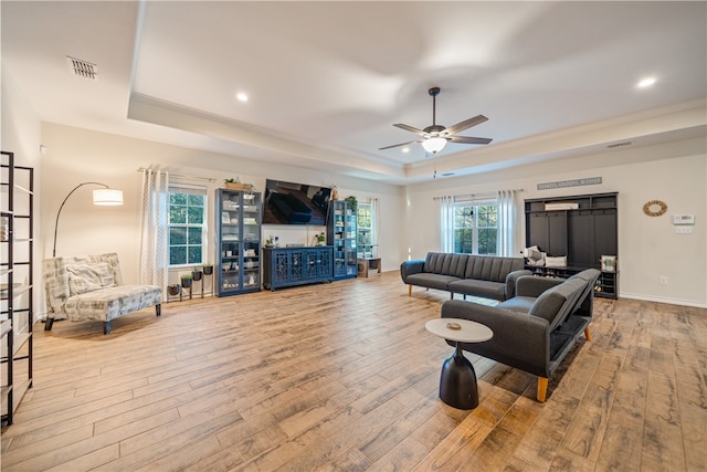 living room with a raised ceiling, ceiling fan, light hardwood / wood-style flooring, and crown molding