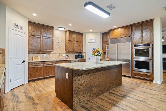 kitchen with tasteful backsplash, light stone counters, stainless steel appliances, light hardwood / wood-style flooring, and a kitchen island