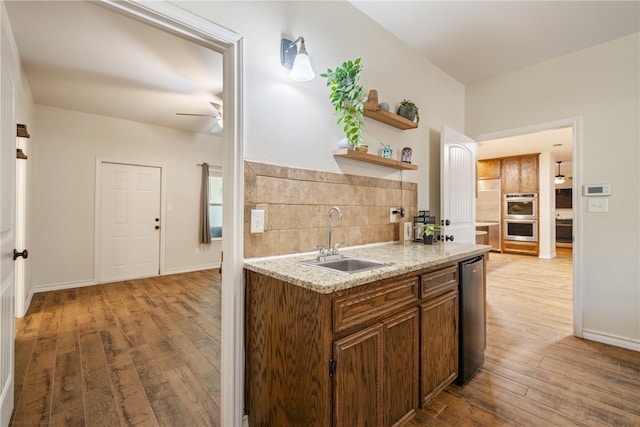 kitchen with tasteful backsplash, ceiling fan, double oven, sink, and light hardwood / wood-style floors