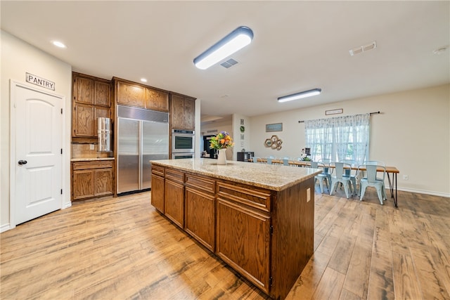 kitchen featuring a kitchen island, light stone countertops, light hardwood / wood-style floors, and stainless steel appliances