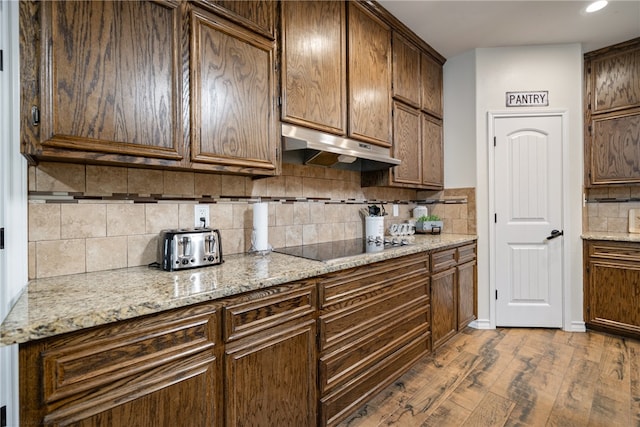 kitchen featuring tasteful backsplash, light stone counters, light hardwood / wood-style flooring, and black electric stovetop