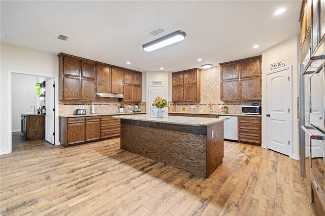 kitchen with light stone counters, light hardwood / wood-style floors, decorative backsplash, a kitchen island, and appliances with stainless steel finishes