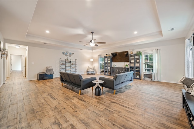 living room featuring a raised ceiling, ceiling fan, and light wood-type flooring