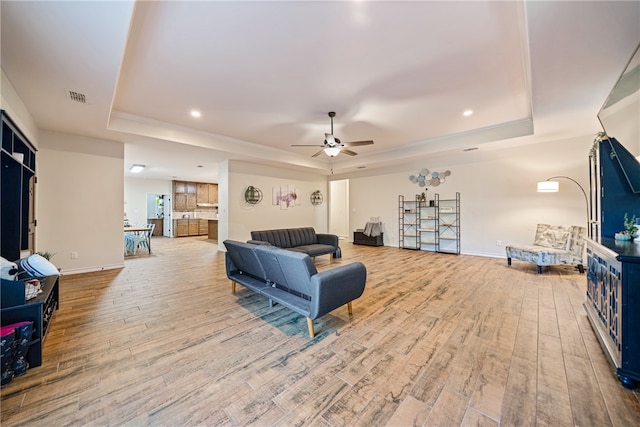 living room featuring a tray ceiling, ceiling fan, and light hardwood / wood-style flooring