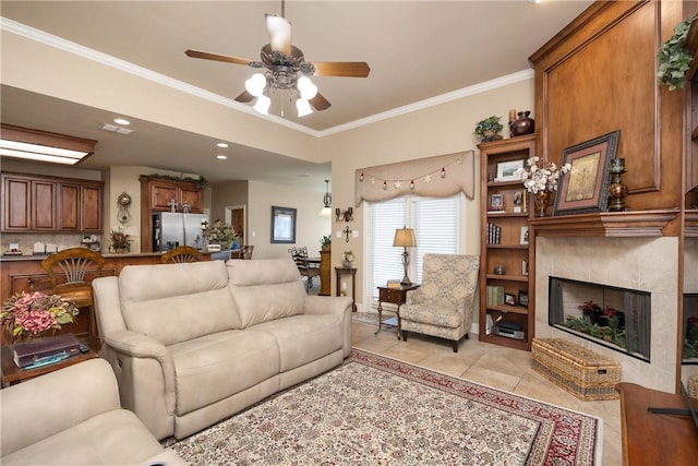 living room with a large fireplace, ceiling fan, crown molding, and light tile patterned floors