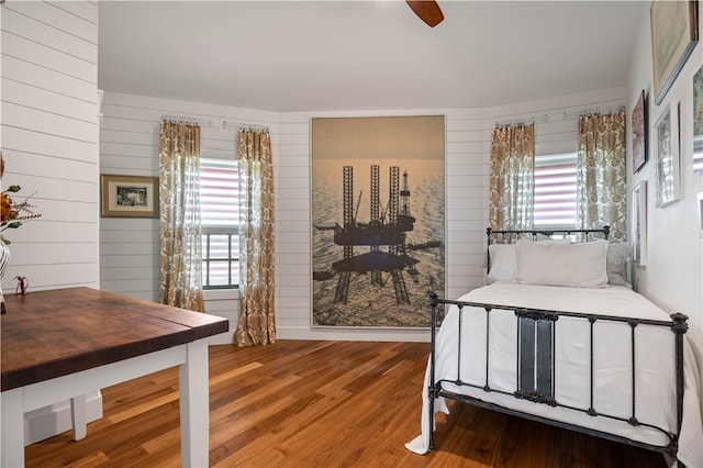 bedroom with multiple windows, ceiling fan, wood-type flooring, and wood walls