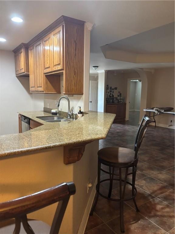 kitchen featuring sink, stainless steel dishwasher, light stone countertops, a kitchen bar, and kitchen peninsula