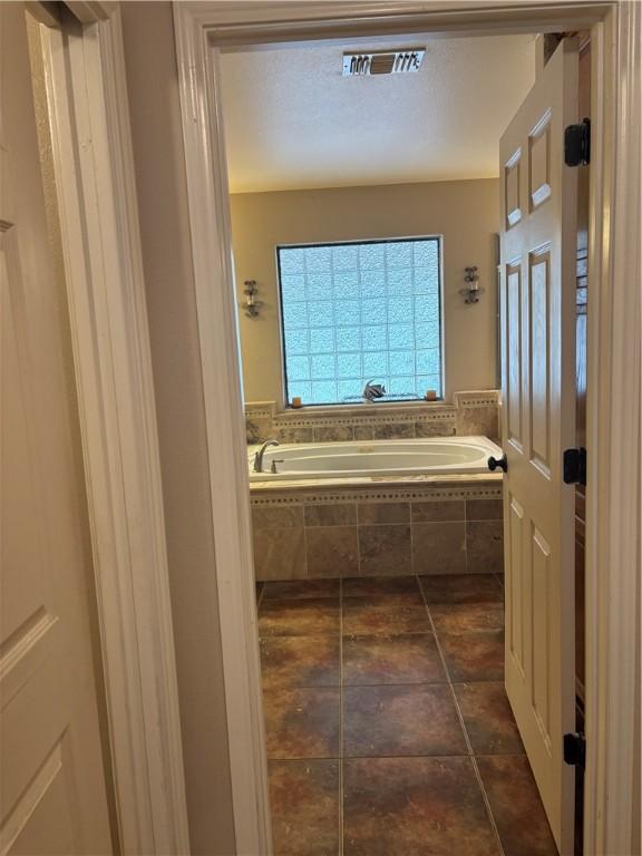 bathroom with tile patterned floors and a relaxing tiled tub