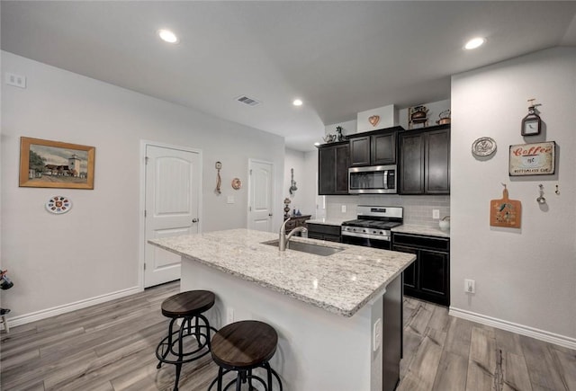 kitchen with light stone counters, an island with sink, light hardwood / wood-style floors, a breakfast bar area, and appliances with stainless steel finishes