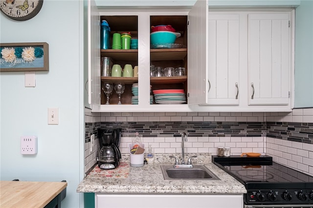 kitchen featuring tasteful backsplash, black stove, light stone counters, white cabinetry, and sink