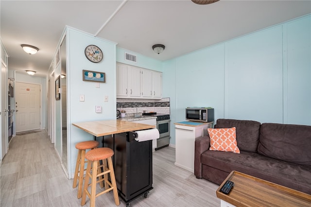 kitchen with stainless steel appliances, kitchen peninsula, a kitchen bar, backsplash, and white cabinets