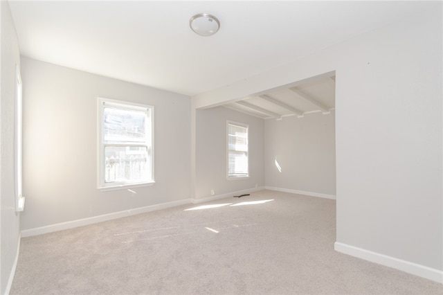 unfurnished room featuring beam ceiling, light colored carpet, and a wealth of natural light