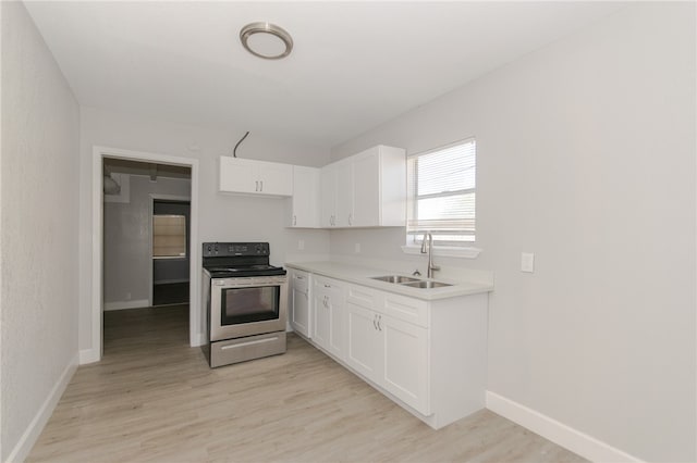 kitchen with electric range, sink, white cabinets, and light hardwood / wood-style flooring