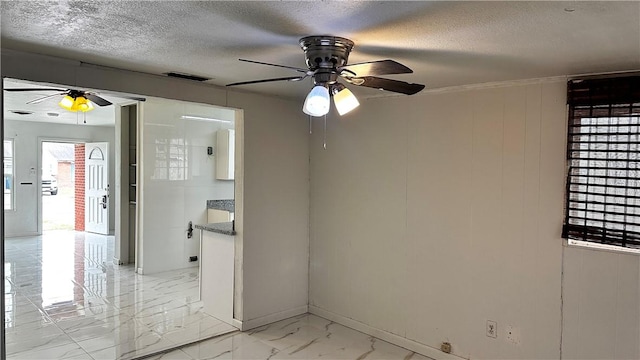 empty room featuring a textured ceiling, marble finish floor, ceiling fan, and baseboards